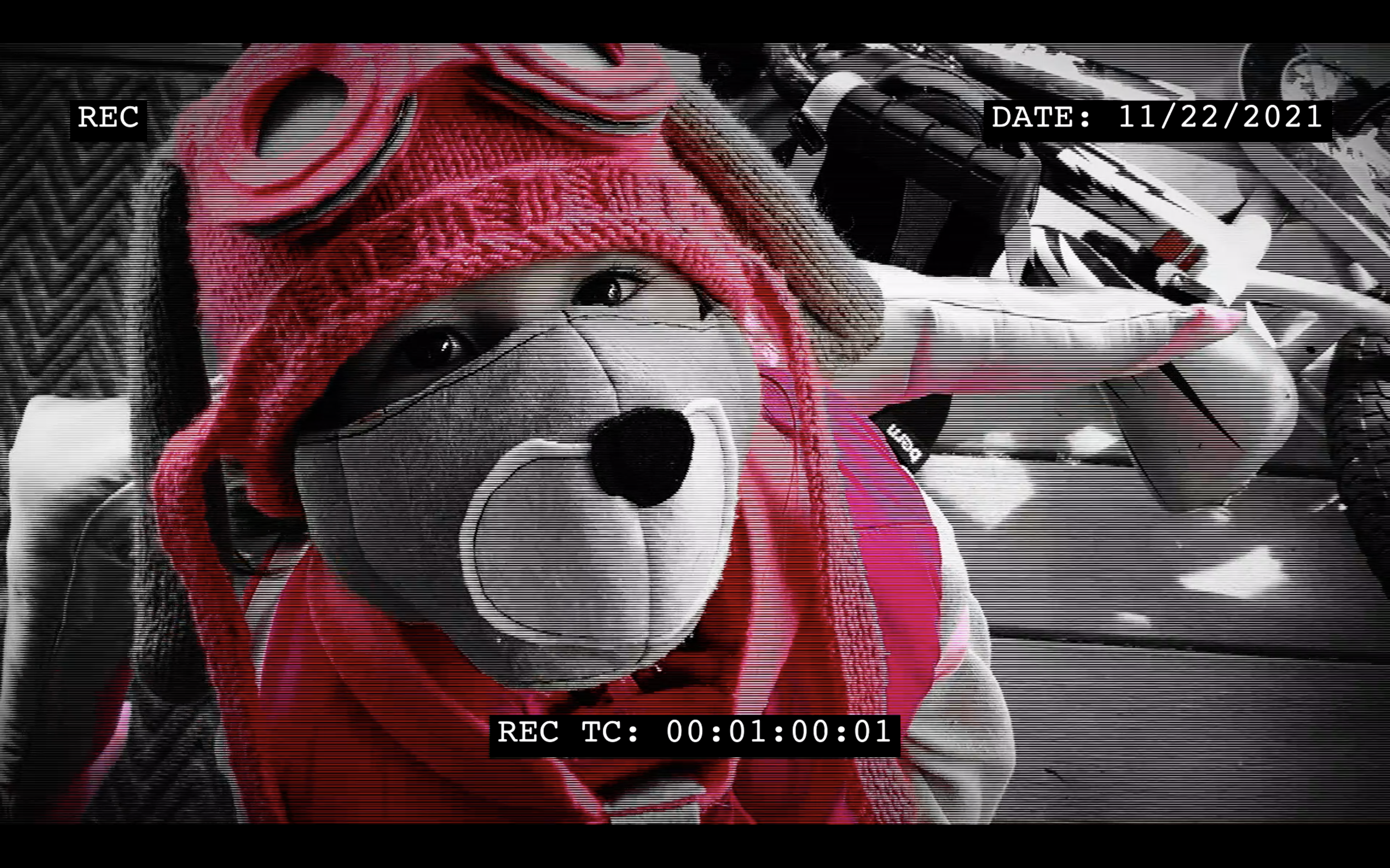 screen capture from video. a girl in pink looking up into video camera in a black and white background